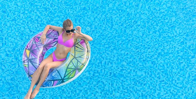 Eine Frau in einem pinken Bikini sitzt in einem Pool in einem bunten Poolfloatie