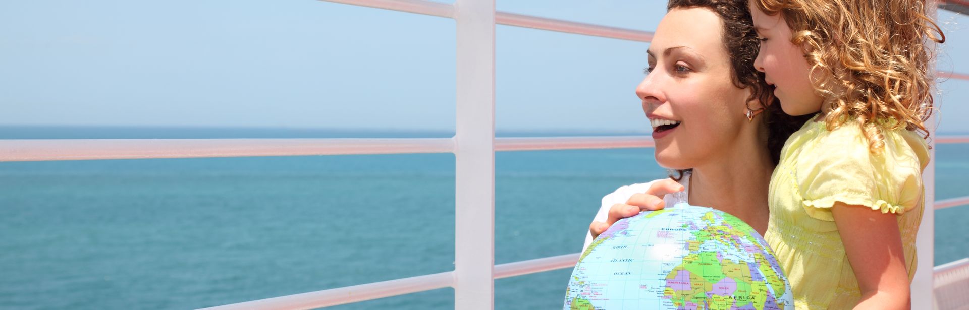 Mutter und Kind schauen über das Geländer eines Kreuzfahrtschiffes und halten einen Globus