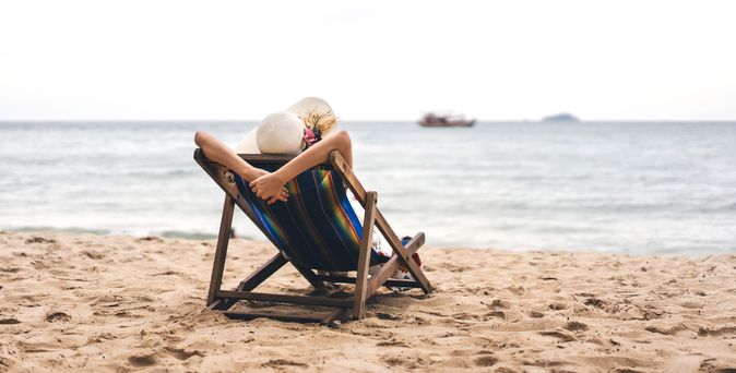 Person am Strand auf einer Liege schaut auf das Meer