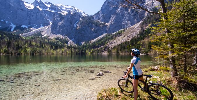 Eine Frau bestaunt auf dem Fahrrad Berge und einen See