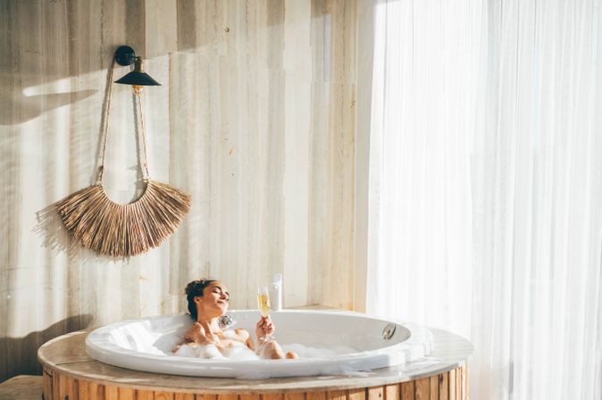 Eine Frau sitzt in einem Whirlpool in einem modernen Hotelzimmer und trinkt ein Glas Sekt