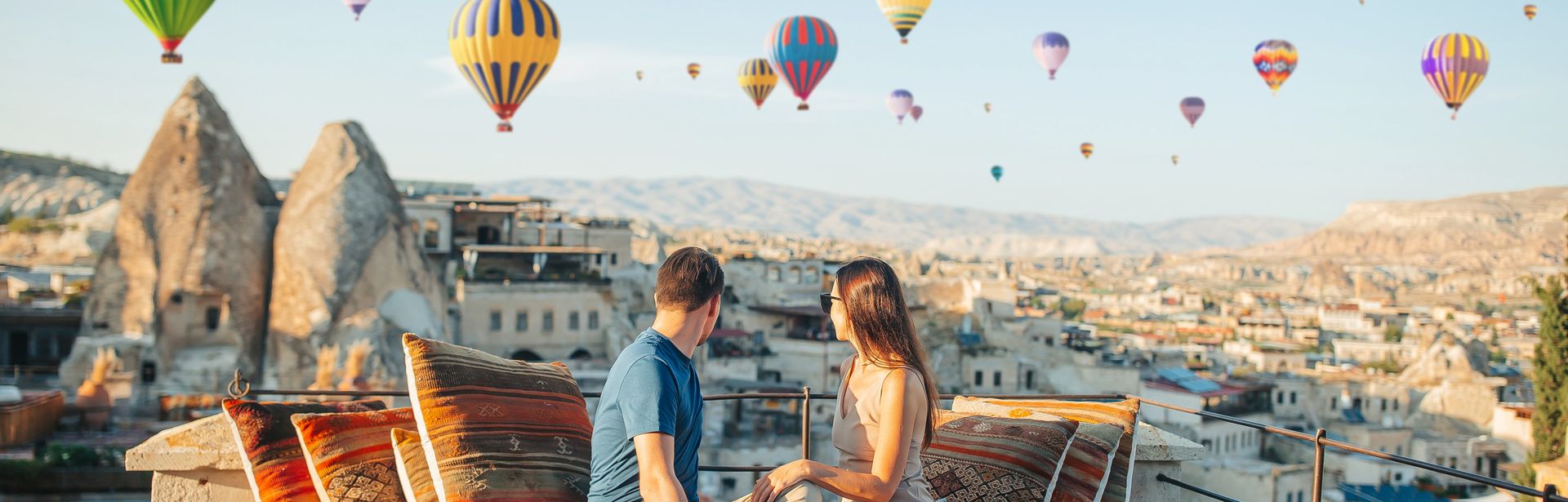 Fröhliches junges Paar beim Sonnenaufgang mit Heißluftballons in Kappadokien