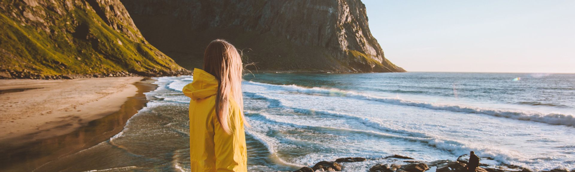 Eine Frau in einer gelben Regenjacke schaut auf das Meer
