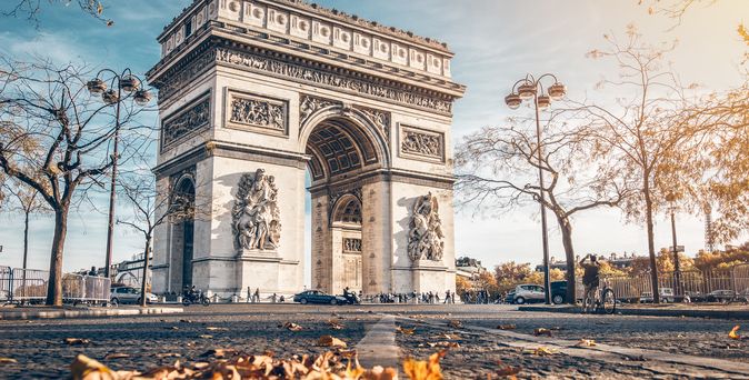 Der Arc de Triomphe im Herbst. im Vordergrund liegen braune Blätter auf dem Boden.
