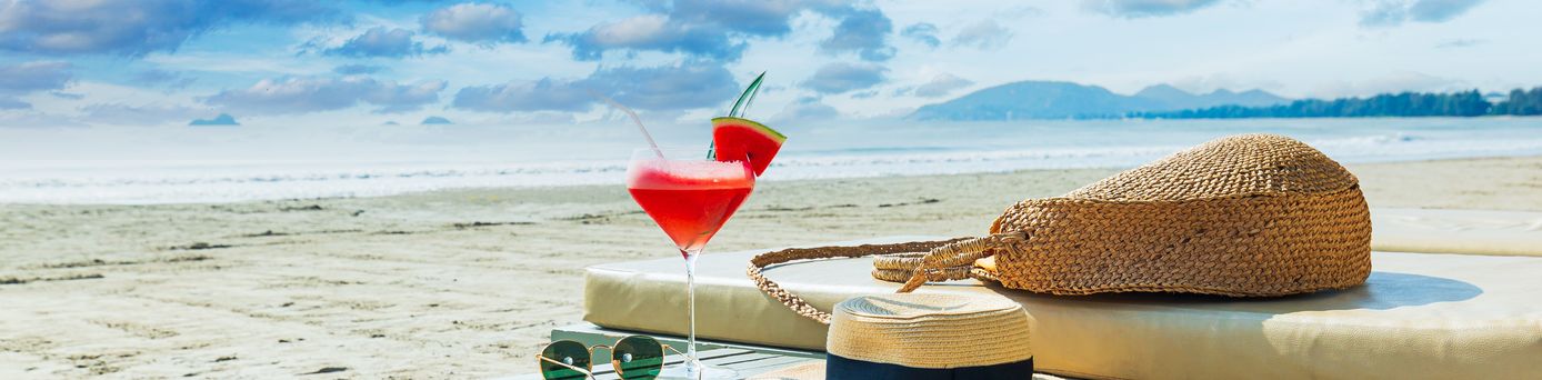 Eine Liege und ein Tisch mit einem Sonnenhut und einem Getränk am Strand