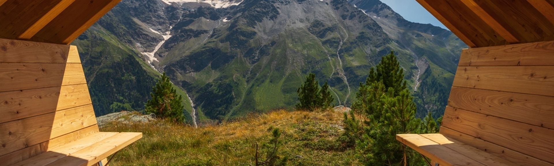 Aus einer Holzhütte mit zwei Bänken schaut man auf eine beeindruckende Berglandschaft