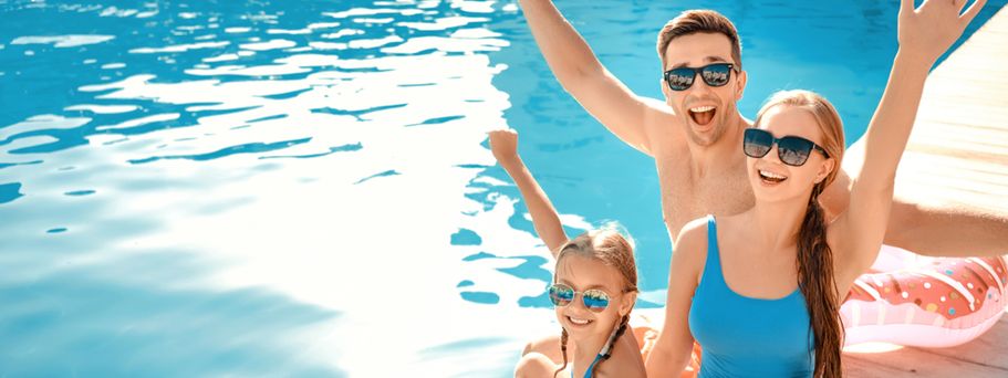 Eine Familie sitzt auf einem Steg und hält lächelnd die Arme in die Luft