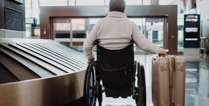 Mann im Rollstuhl schiebt seinen Koffer am Flughafen