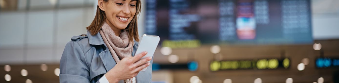 Frau am Flughafen schaut lächelnd auf ihr Smartphone