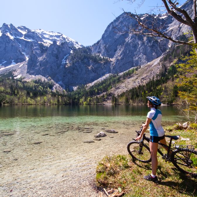 Eine Frau bestaunt auf dem Fahrrad Berge und einen See