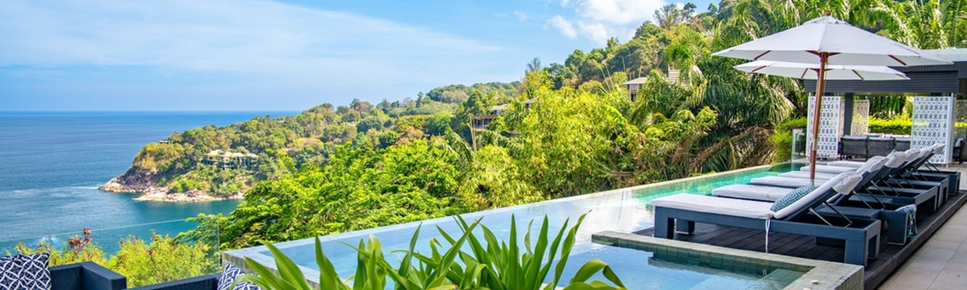 Ein eleganter Infinity Pool umgeben von Ledersofas, Liegen und Pflanzen mit Blick auf das Meer
