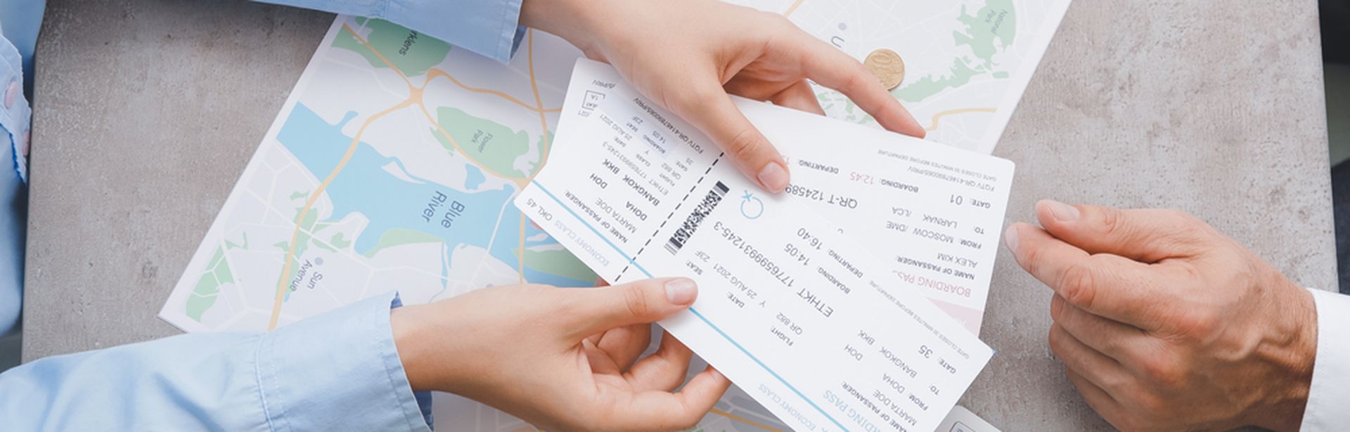 Auf einem Tisch liegen eine Landkarte, ein Taschenrechner, ein Reisepass und eine Geldbörse. Zwei Paar Hände sind zu sehen, ein Paar Hände hält Flugtickets