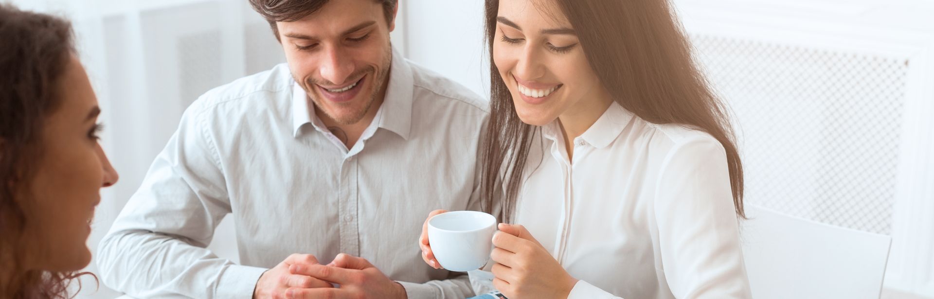 Ein Paar sitzt mit einer Reiseberaterin am Tisch, während die Reiseberaterin ihnen etwas auf einer Karte auf dem Tisch zeigt