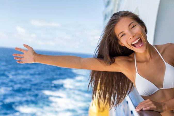 Eine Frau auf einem Kreuzfahrtschiff streckt lachend ihren Arm aus