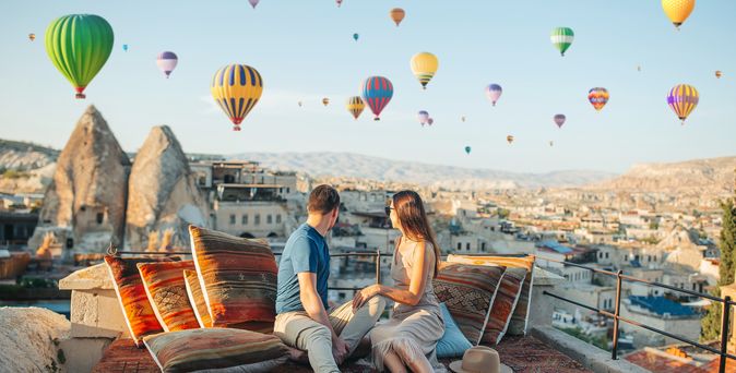 Fröhliches junges Paar beim Sonnenaufgang mit Heißluftballons in Kappadokien