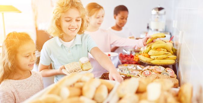 Vier Kinder bedienen sich lächelnd an einem Frühstücksbuffet