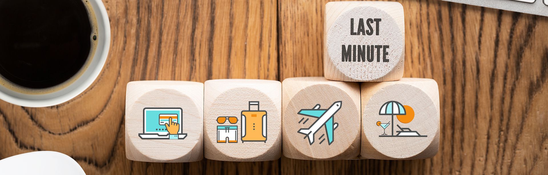 Auf einem Schreibtisch liegen Holzwürfel mit Symbolen drauf in einer Reihe und einem darüberliegenden Würfel, wo "Last Minute" drauf steht