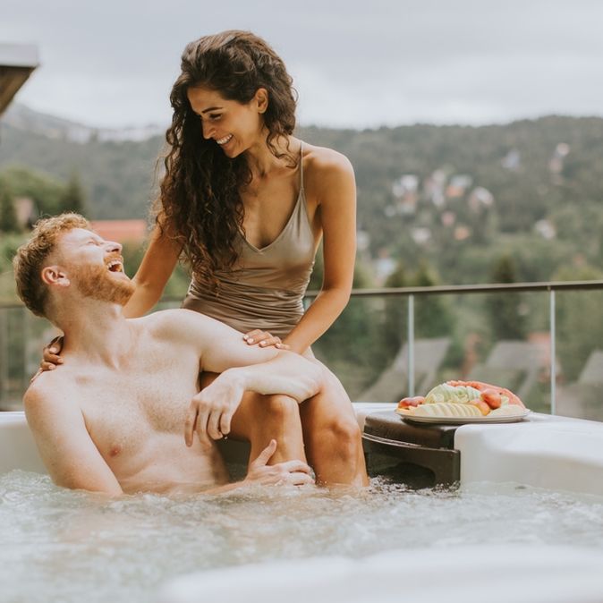 Ein Mann sitzt im Whirlpool und eine Frau sitzt hinter ihm auf dem Rand des Whirlpools