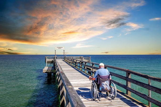 Mann im Rollstuhl auf einer Seebrücke am Meer