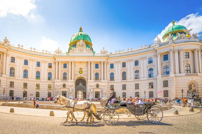 Pferdekutsche vor der Hofburg in Wien, Österreich, an einem sonnigen Tag. Im Hintergrund laufen viele Touristen über den Platz.