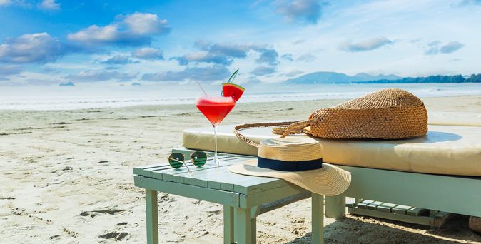 Eine Liege und ein Tisch mit einem Sonnenhut und einem Getränk am Strand