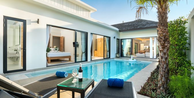 Ein Pool vor einer eleganten Villa mit zwei Liegen und einem Tisch