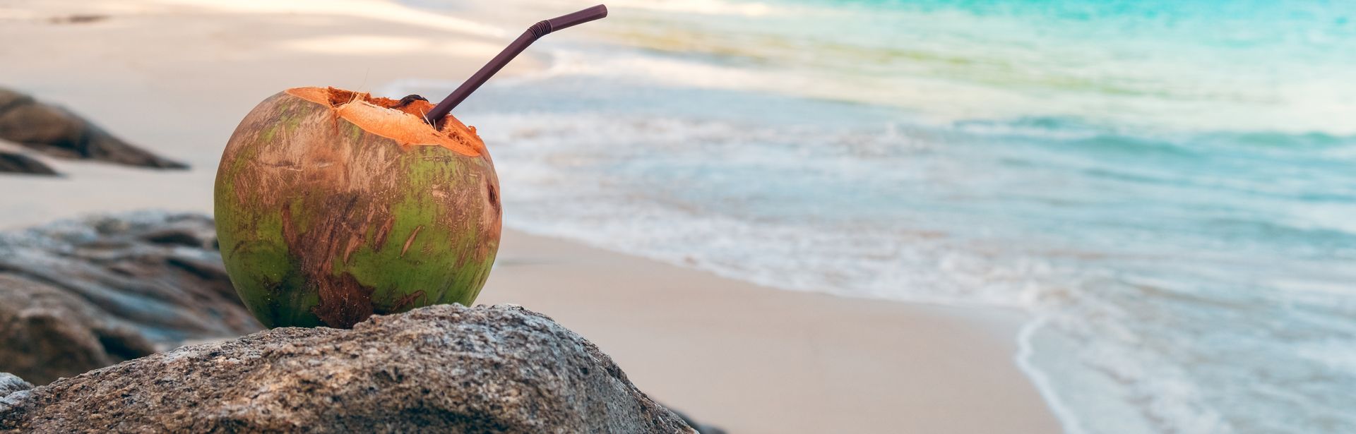 Eine Kokosnuss mit Strohhalm liegt auf Steinen an einem wunderschönen Strand