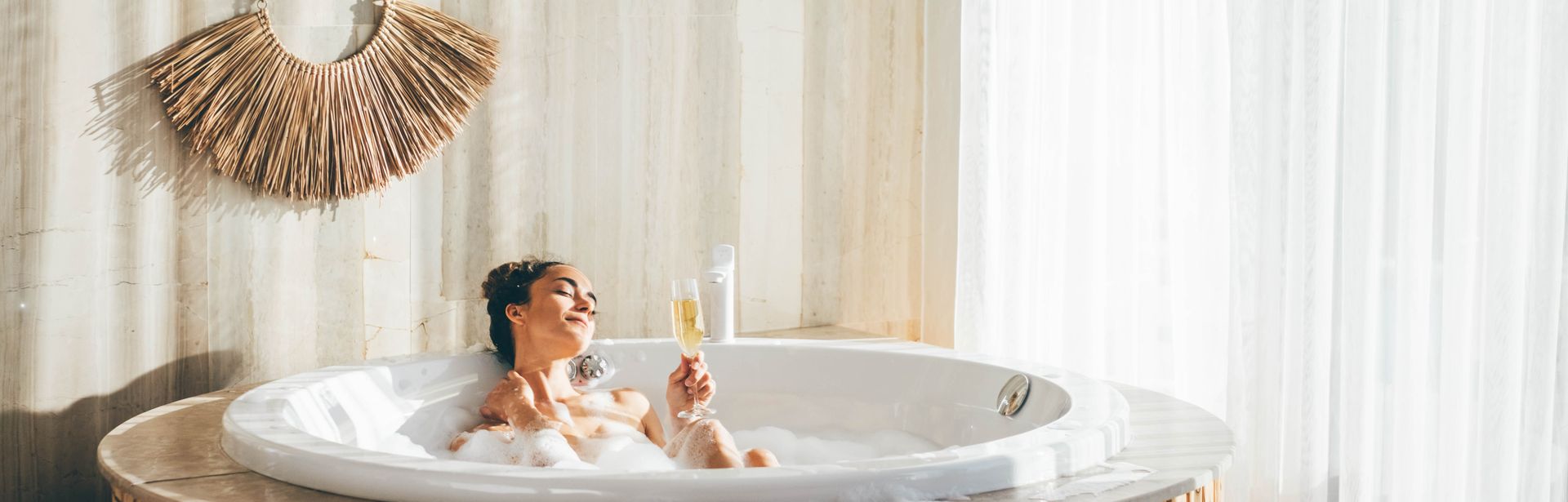 Eine Frau sitzt in einem Whirlpool in einem modernen Hotelzimmer und trinkt ein Glas Sekt