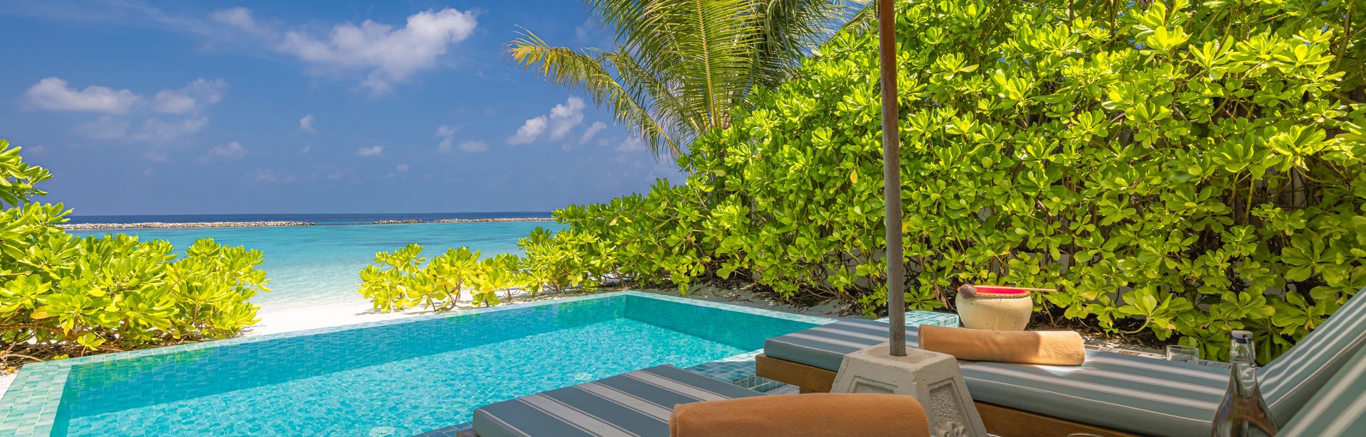 Zwei Liegen unter einem Sonnenschirm, vor einem kleinen Pool