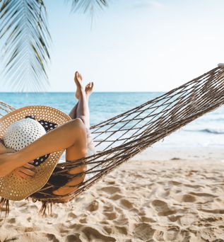 Frau mit Sonnenhut entspannt in einer Hängematte am Strand