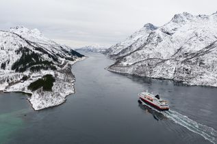 Ein Kreuzfahrtschiff fährt durch einen Fjord, umgeben von schneebedeckten Bergen und winterlicher Landschaft.