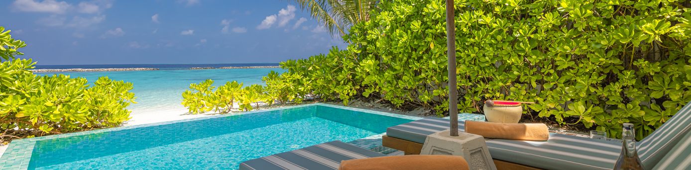 Zwei Liegen unter einem Sonnenschirm, vor einem kleinen Pool