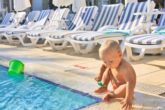 Ein Kleinkind sitzt am Rand eines Pools und spielt mit einer Spielzeugschaufel