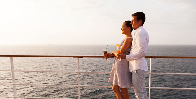 Ein Paar steht auf einem Kreuzfahrtschiff an der Reling und schaut aufs Meer