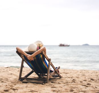 Person am Strand auf einer Liege schaut auf das Meer