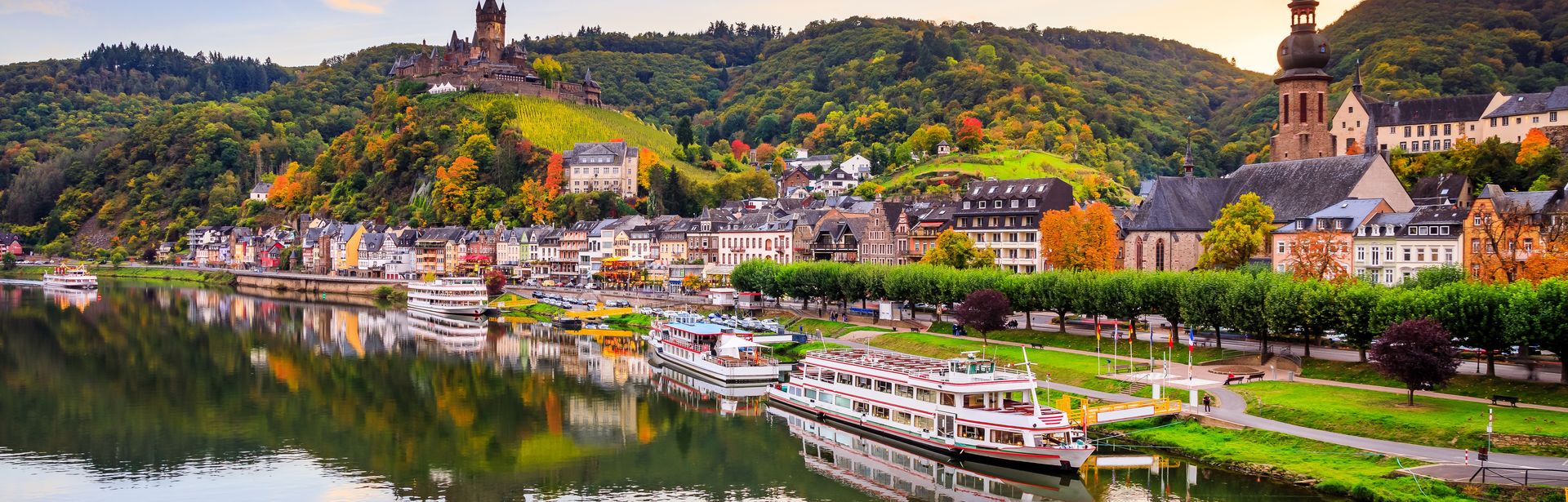 Schiffe am Ufer der Mosel mit Häusern und Sonnenuntergang im Hintergrund