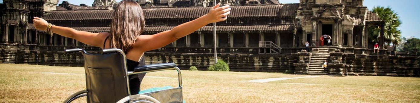 Frau im Rollstuhl vor einem Tempel und hebt die Arme