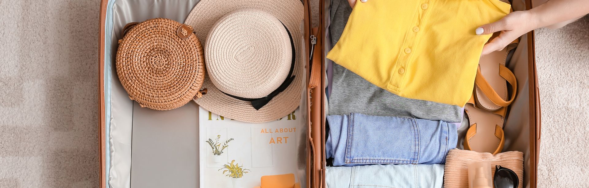 Ein Koffer wird gepackt auf einem Teppich. Ein Paar Hände legt einen gefalteten Pulli in den Koffer