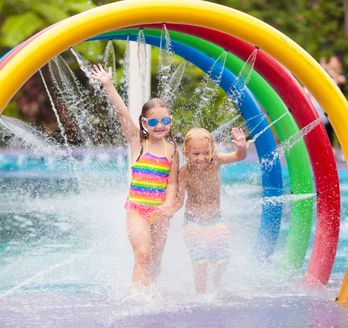 Zwei Kinder laufen durch Bunte Bögen aus denen Wasser auf sie gespritzt wird