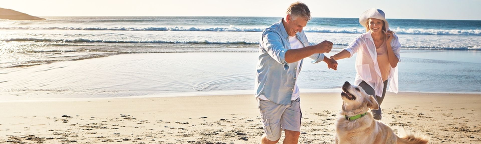 Eine Frau und ein Mann spielen am Strand mit einem Hund 