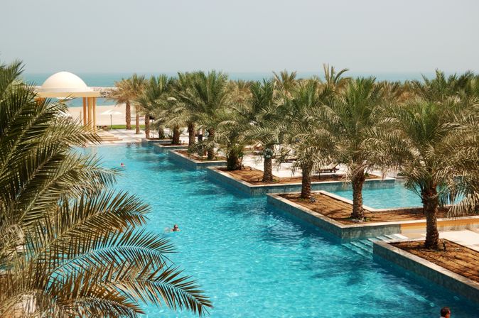 Poollandschaft mit Palmen und Blick auf das Meer