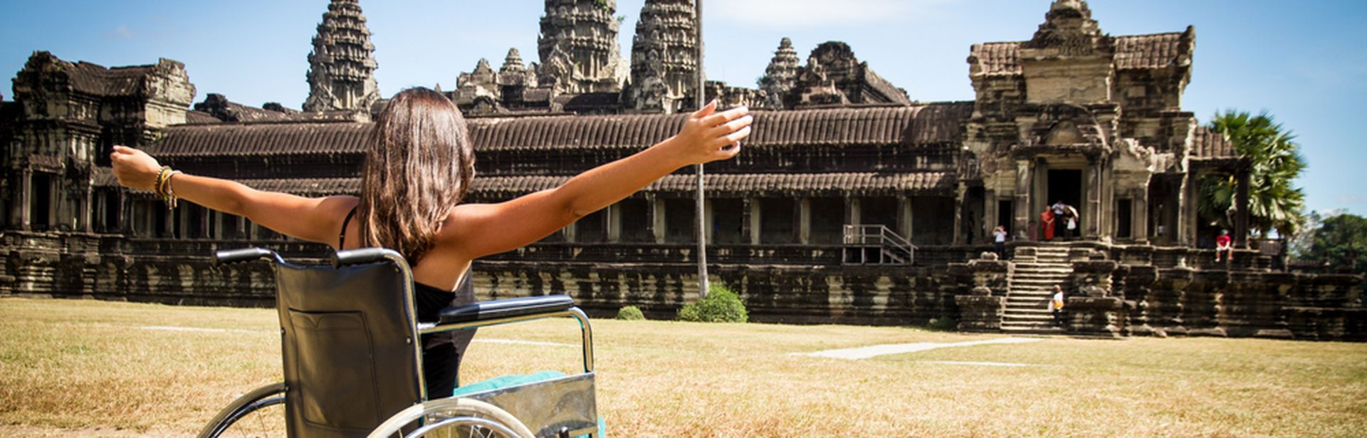 Frau im Rollstuhl vor einem Tempel und hebt die Arme
