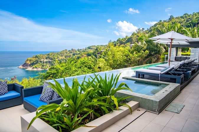 Ein eleganter Infinity Pool umgeben von Ledersofas, Liegen und Pflanzen mit Blick auf das Meer