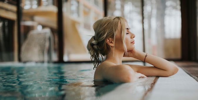 Frau lehnt am Rand eines indoor Pools und hat die Augen geschlossen