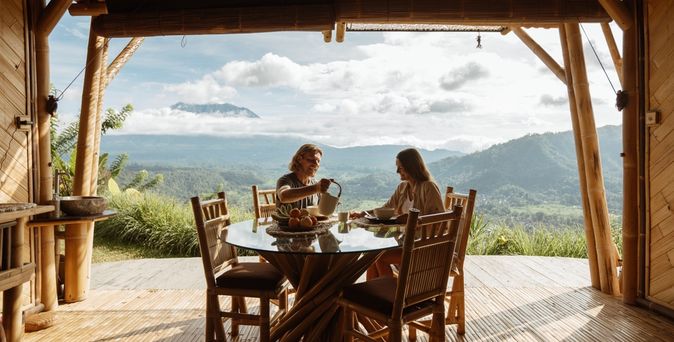 Auf einer Terrasse mit beeindruckendem Ausblick auf eine grüne Landschaft sitzen zwei Personen an einem Tisch 