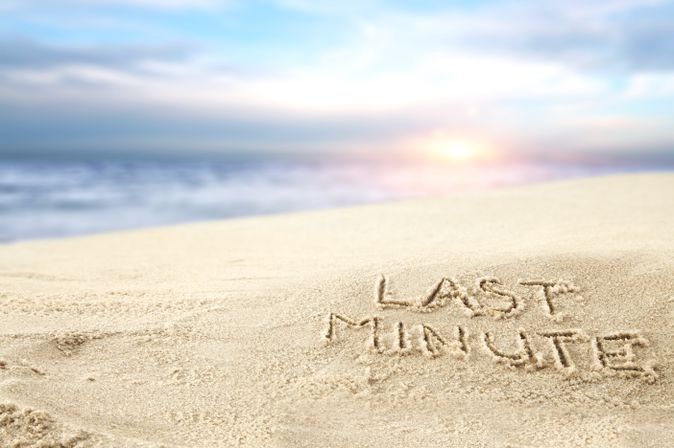 Ein Sonnenuntergang am Strand, im Sand steht "Last Minute" geschrieben