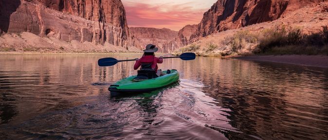 Eine Person sitzt in einem grünen Kanu und schaut auf einen pinken Sonnenauf/untergang