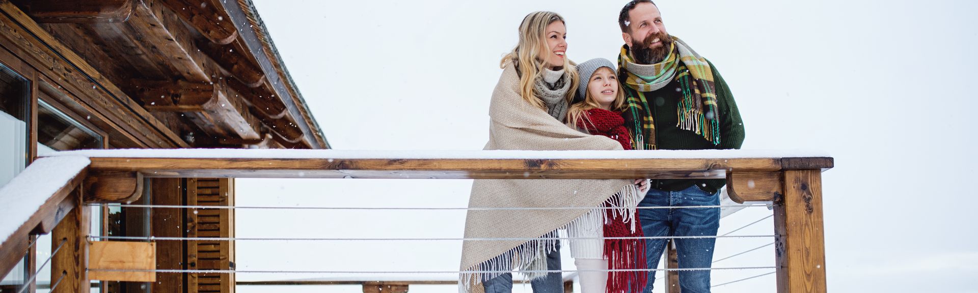 Eine Familie steht in Decken gehüllt auf dem Balkon Ihres Hotels im Schnee