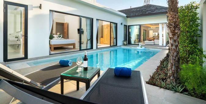 Ein Pool vor einer eleganten Villa mit zwei Liegen und einem Tisch