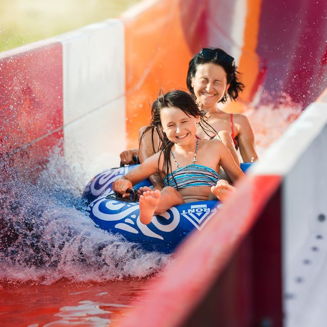 Eine Frau und ein Kind rutschen auf einem Reifen eine rote Wasserrutsche